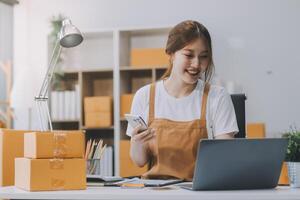 Starting Small business entrepreneur SME freelance, Portrait young woman working at home office, BOX, smartphone, laptop, online, marketing, packaging, delivery, b2b, SME, e-commerce concept.. photo