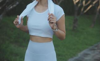 joven hembra rutina de ejercicio antes de aptitud formación sesión a el parque. sano joven mujer calentamiento arriba al aire libre. ella es extensión su brazos y mirando lejos, hola llave. foto