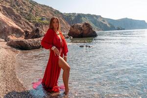 Beautiful sensual woman in a flying red dress and with long hair, stands on the seashore photo