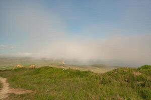 A foggy day with a cloudy sky and a grassy hill. The sky is blue and the clouds are white. photo