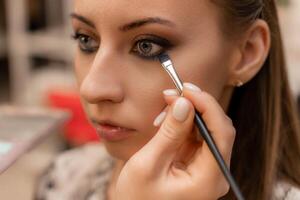 Make-up artist working with brush on model eyes Close up of applying make up on young girl,semi profile, professional make up in beauty studio photo