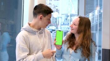 joven milenario amigos sentado fuera de con café y mirando a verde pantalla teléfono en parque. contento sonriente personas utilizando moderno teléfono inteligente tecnología. medios de comunicación, estilo de vida, Internet educación concepto video