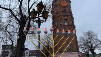 Hanukkah lights glow against the backdrop of a winter city of bare trees and sky lanterns close up of Hanukkah Doughnuts being sprinkled with powdered sugar in slow motion video