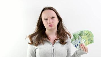 insatisfecho trastornado niña con un taco de euro dinero, 100 euro factura, picaduras su labios, frunce el ceño su frente, mira dentro el marco en enojo, es trastornado porque dinero lo hace no media felicidad el Rico además llorar video