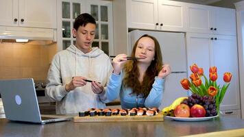 heerlijk sushi leren naar eten met eetstokjes tonen elk andere dwaas in de omgeving van Speel jongen en meisje tieners in keuken aan het kijken film Aan laptop en aan het eten lunch lunch eerste datum vermaak fruit bloemen video