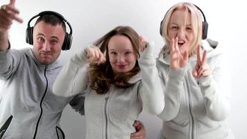 alegre familia en auriculares bailando demostración pulgares arriba en contra el antecedentes de blanco chándales teniendo divertido familia Deportes gasto hora juntos contento familia mamá hija padre alegre música video