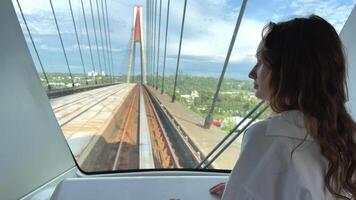 European girl with blond long hair in a white shirt rides in a skytrain She looks into the windshield of a driverless train passing over a bridge in Vancouver Canada video