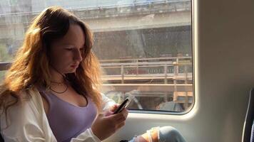 là est espace pour texte ukrainien juste aux cheveux européen fille est assis dans skytrain et elle écoute à la musique dans de face de sa détient le téléphone elle est dans une blanc chemisier et bleu déchiré jeans elle est dans une tunnel video