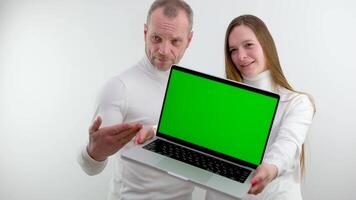 serious adult man and girl showing a laptop screen with his hand space for advertising text Green background chroma key white background white clothes clean gods make the world a better place video