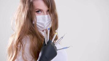 Beautiful woman dentist in a white suit with a white mask with flowing hair holds in her hands scaler and curette Hand stretched forward selective focus bright photo of gorgeous woman video