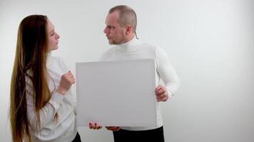 Young happy couple portrait of a confident businessman showing presentation, pointing paper placard gray background. Ideal for banners, registration forms, presentation, landings, presenting concept. video