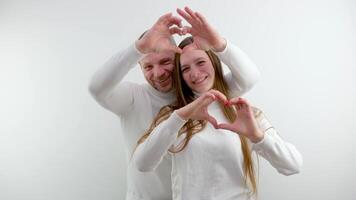 make a heart with hands man and woman in love stand on a white background Light clothes two hands make a heart smile laugh space for text valentine's day wedding tenderness different ages video