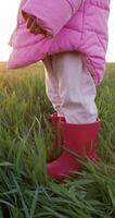 bambino ragazza gambe nel stivali su il azienda agricola campo con tramonto luce. verticale metraggio video