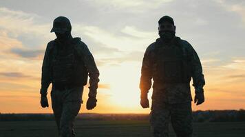 soldater stående förenad på skymning, två soldater lämna tillbaka på solnedgång och promenad ett huvud, de solnedgång Bakom dem. video
