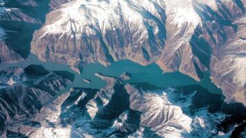 arial Visão do uma montanha lago entre Nevado picos, Alto altitude aéreo Visão do uma profundo azul montanha lago cercado de coberto de neve picos, oferta uma deslumbrante natural panorama a partir de acima. video