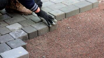 lavoratore posa pavimentazione pietre, avvicinamento di un' lavoratori mani posa grigio pavimentazione pietre su un' strada, indossare guanti. video