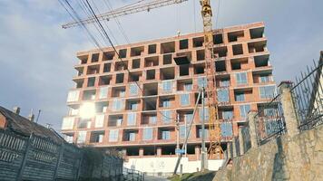 moderno urbano construcción sitio debajo desarrollo, un grande de varios pisos edificio debajo construcción en un urbano configuración, presentando un imponente grua y inconcluso ladrillo fachada tomando el sol en luz de sol. video