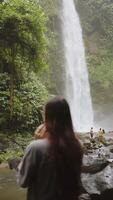 flicka leende i främre av tropisk vattenfall, vertikal video