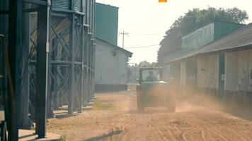Tractor Driving in Dusty Farmyard, a tractor driving through a dusty farmyard, surrounded by farm buildings and equipment. video