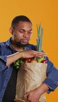 vertikal Lycklig ung man reklam organisk lokalt vuxen frukt och grönsaker, presenter en bio kemikalier fri morot i studio. nöjd person stöder friska äter och veganism. kamera b. video