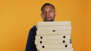 klumpig deliveryman dropp en enorm stack av pizza lådor i studio, slöseri en massa av mat och framställning en röra. ung bedrövad man gör en misstag och spill en stor lugg av snabb mat. kamera a. video