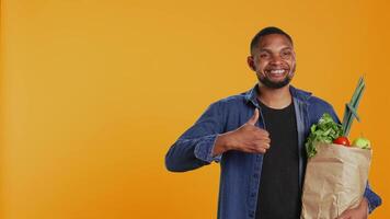 Cheerful positive guy giving a thumbs up for locally grown produce, advocating for zero waste and healthy eating from farmers market. Young adult doing a like gesture in studio. Camera B. video