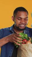vertical feliz jovem homem publicidade orgânico localmente crescido frutas e legumes, apresentando uma bio produtos químicos livre cenoura dentro estúdio. satisfeito pessoa apoia saudável comendo e veganismo. Câmera uma. video