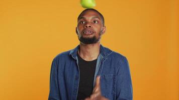 Playful person juggling in the studio with ripe green apples, keeping it in the air with continuous motion by throwing and catching. Confident skilled guy having fun with organic fruits. Camera A. video