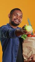 verticale africano americano uomo presentazione un' appena raccolto verde mela, mostrando il biologico bio frutta nel davanti di il telecamera. contento persona sostenendo per salutare mangiare e vegano nutrizione. telecamera b. video