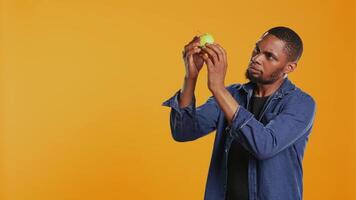 Male model examining a green apple to be clean after harvesting, guaranteeing the ripeness of locally grown fruits. Young adult supporting sustainable lifestyle concept. Camera B. video