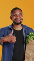 Vertical Cheerful positive guy giving a thumbs up for locally grown produce, advocating for zero waste and healthy eating from farmers market. Young adult doing a like gesture in studio. Camera B. video