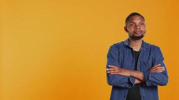 Porträt von afrikanisch amerikanisch beiläufig Mann posieren gegen Orange Hintergrund, zeigen Vertrauen und Entschlossenheit im Studio. charismatisch ernst Kerl im stilvoll Kleidung. Kamera b. video