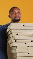 Vertical Clumsy deliveryman dropping a huge stack of pizza boxes in studio, wasting a lot of food and making a mess. Young distressed man makes a mistake and spills a large pile of fast food. Camera B. video