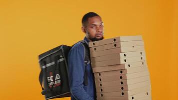 Reckless mad deliveryman spilling a lot of pizza in studio, dropping massive stack of boxes and making a mess. Male courier being clumsy and causing an accident during takeaway service. Camera B. video