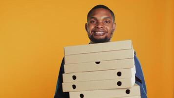 africano americano pizzeria fattorino Tenere pila di Pizza scatole per consegnare cibo ordine per cliente nel studio. amichevole portare fuori servizio dipendente trasporta porta via pasto pacchetto. telecamera un. video