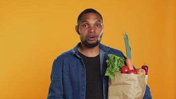 Confident man juggling with an eco friendly green apple on camera, presenting ripe locally grown fruits. Young adult playing around and carrying paper bag with organic produce. Camera A. video