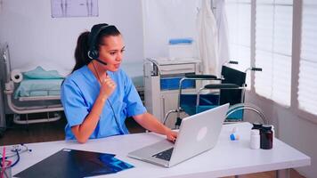 Surgeon assistant using headphones in hospital answering to patients calls for appointments and consultations. Healthcare physician in medicine uniform, doctor nurse helping with telehealth communication video