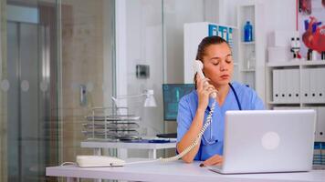 Medical staff talking with patient on phone from hospital about diagnosis, male nurse working in background. Healthcare physician, receptionist doctor assistant helping with telehealth communication video