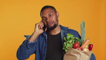 African american man on grocery shopping spree chatting on phone call, discussing with people about a new zero waste eco store in the city. Young adult recommends fresh bio produce. Camera A. video
