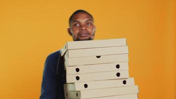Afrikaanse Amerikaans pizzeria koerier draagt stapel van pizza dozen voor uitdrukken levering, geven voedsel bestellen naar klant. vriendelijk meenemen onderhoud werknemer Holding afhaalmaaltijd maaltijd pakket. camera a. video
