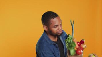 mannetje persoon spelen in de omgeving van met een groen appel in studio, tonen zijn jongleren vaardigheden terwijl hij draagt zak gevulde met etisch afkomstig voedsel produceren. veganistisch vent aanbevelen biologisch vruchten. camera a. video