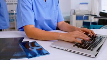 cerca arriba de médico mujer enfermero escritura resultados de paciente radiografía, mecanografía en ordenador portátil sentado en hospital. radiólogo en médico uniforme mirando a radiografía, examen, hueso, analizar, diagnóstico. video