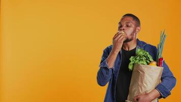 afrikansk amerikan vegan kille tar en bita från en mogen naturlig grön äpple, äter nyligen UPPTAGITS organisk frukt i studio. person reklam lokal- jordbruk och etiskt kommer från varor. kamera b. video