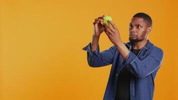 Young man inspecting a freshly harvested green apple in studio, making sure its clean and ripe for consuming. Vegan person examines organic fruits from local zero waste eco store. Camera B. video