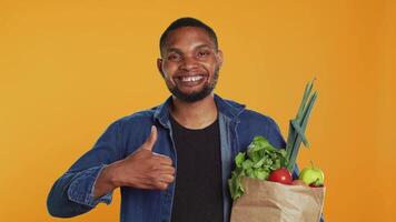 Cheerful positive guy giving a thumbs up for locally grown produce, advocating for zero waste and healthy eating from farmers market. Young adult doing a like gesture in studio. Camera A. video