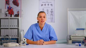 Authentic experienced woman nurse talking to camera and giving online medical consultation from private modern clinic. Remote healthcare service, health conference, telemedicine, virtual meeting video
