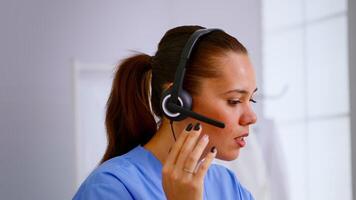Portrait of medical receptionist answering pressing on headphone helping patient making appointment in hospital. Healthcare physician in medicine uniform, doctor assistant during telehealth communication video