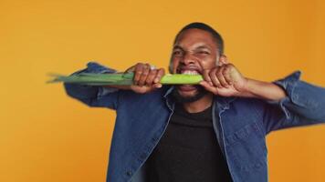 Young person biting on a green onion and acting silly in studio, pretending to eat a natural ethically sourced leek to advocate for sustainable lifestyle and veganism. Camera A. video