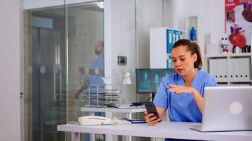 kvinna sjuksköterska innehav smartphone talande till patient framställning telemedicin uppkopplad ringa upp. terapeut avlägsen samråd i telefonkonferens virtuell mobil chatt Ansökan, telehälsa begrepp video