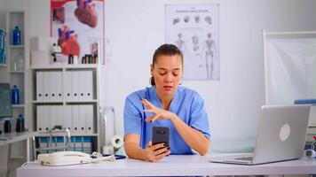 ervaren vrouw verpleegster geven online medisch overleg gebruik makend van smartphone van privaat modern kliniek. afgelegen gezondheidszorg onderhoud, Gezondheid conferentie, telegeneeskunde, virtueel vergadering video